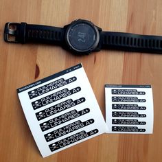 a watch sitting on top of a wooden table next to some paper and stickers