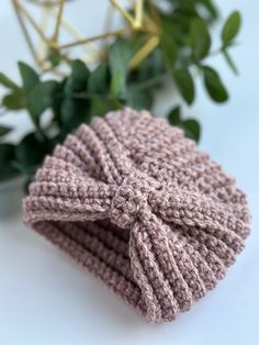 a crocheted hat with a bow on the side sitting next to a plant