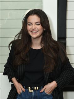 a woman standing in front of a white wall with her hands on her hips and smiling at the camera