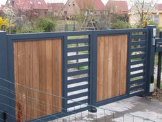 a wooden gate with metal bars on the top and bottom part, in front of some houses