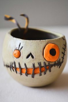 a ceramic bowl with painted faces and orange eyes on it's sides, sitting on a white surface