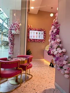 the interior of a flower shop with pink chairs and flowers hanging from the wall behind them