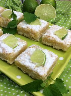 several pieces of cake with limes and powdered sugar on top sitting on a green plate