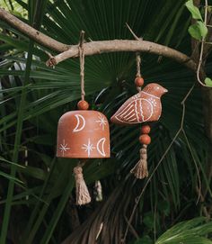 two clay birds hanging from a tree branch with moon and stars painted on the bells