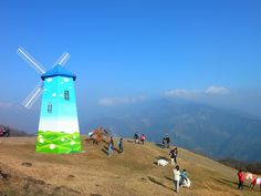 many people are standing on the top of a hill with a windmill in the background