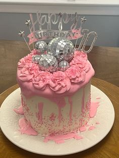 a birthday cake with pink frosting and silver decorations on top is sitting on a table