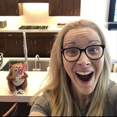 a woman taking a selfie in front of a kitchen sink with a stuffed animal on the counter