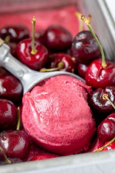 a scoop of ice cream with cherries on it in a metal container next to a spoon