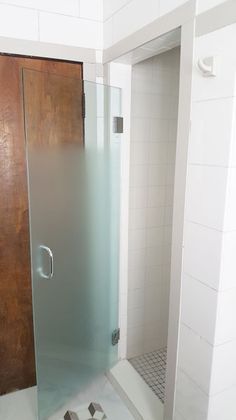 a bathroom with a glass shower door next to a tiled floor and walls, in front of a wooden door