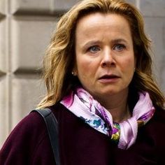 a woman standing next to a building with a handbag on her shoulder and looking off into the distance