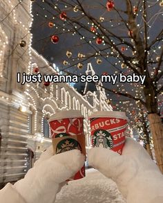 someone holding up two cups of starbucks coffee in front of a christmas tree with lights