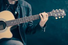 a man is playing an acoustic guitar in front of a black background with his hand on the strings