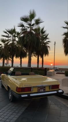 a yellow car parked on the side of a road next to palm trees at sunset