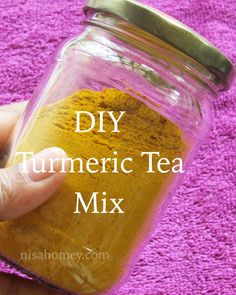 a hand holding a jar filled with tumericic tea mix on top of a purple towel