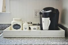 the coffee maker is sitting in the tray on the kitchen counter top next to two mugs