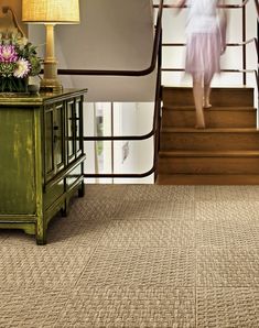 a woman is walking up the stairs in a house with beige carpet and green furniture