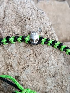 a green and black rope with a silver bead on it next to a rock