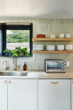 a kitchen with white cabinets and open shelving above the sink is filled with dishes