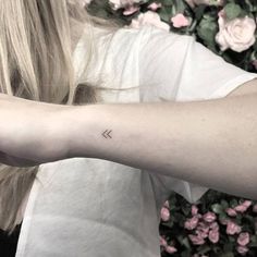 a woman's arm with a small arrow tattoo on the left side of her arm