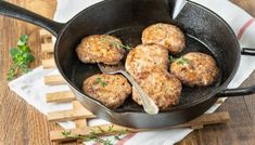 some meat patties are cooking in a skillet on a wooden table with napkins