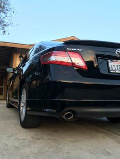 the back end of a black car parked in front of a garage with its door open