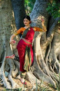 a woman standing in front of a tree with her arms spread out and legs crossed