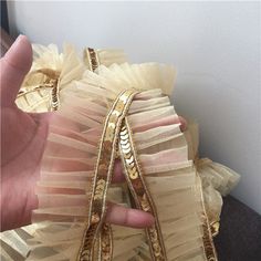 a hand is holding a piece of fabric with gold sequins and ribbons on it