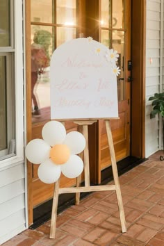 a welcome sign in front of a door with balloons on the side and a flower at the bottom