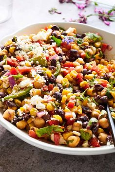 a white bowl filled with black beans, corn and feta cheese next to a glass of water