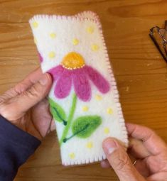 two hands are holding a phone case decorated with flowers and daisies on a wooden table