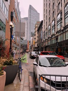 cars parked on the side of a street next to tall buildings and plants in planters