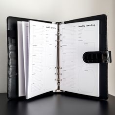 an open planner book sitting on top of a black desk next to a pen and clipboard