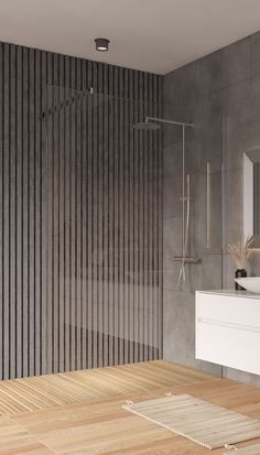 a bathroom with a wooden floor and gray wall covering the shower area, along with a white sink and large mirror