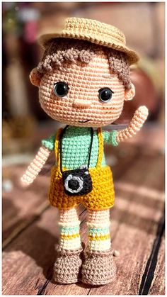 a small crocheted doll with a camera in its hand on a wooden table