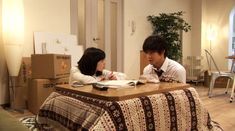 a man and woman sitting at a table with boxes on the floor in front of them