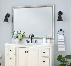 a bathroom vanity with two sinks and a large mirror above it, next to a potted plant