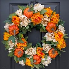 a wreath with pumpkins and flowers on the front door