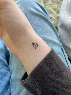 a person with a small black clover tattoo on their left wrist, sitting in the grass