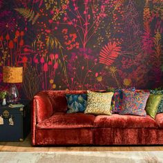 a red couch sitting in front of a wall covered in colorful flowers and foliages