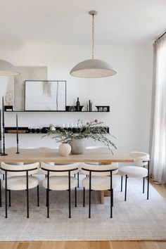 a dining room table with white chairs and hanging lights