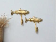 two gold fish hooks on the wall next to a potted plant