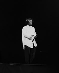 a man standing on top of a stage wearing a white shirt and black pants with a crown on his head