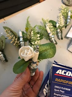 someone is holding a fake white rose with green leaves and some razors next to it