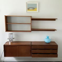 a wooden shelf with two shelves and a blue vase on the top, against a white wall