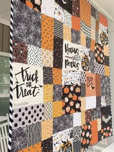 an orange and black patchwork quilt hanging on the side of a white house with words written on it