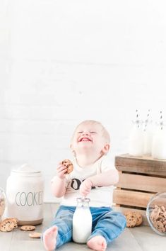 a baby sitting on the floor with cookies and milk