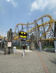 a man is walking in front of the batman coaster at an amusement park with a bat symbol on it