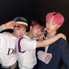 three young men standing next to each other in front of a black wall with pink hair