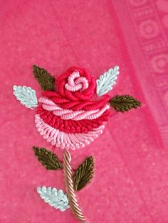 a red rose with green leaves is on a pink background and there are two pins attached to it