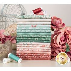 a stack of different colored fabrics next to some pink flowers and a birdcage